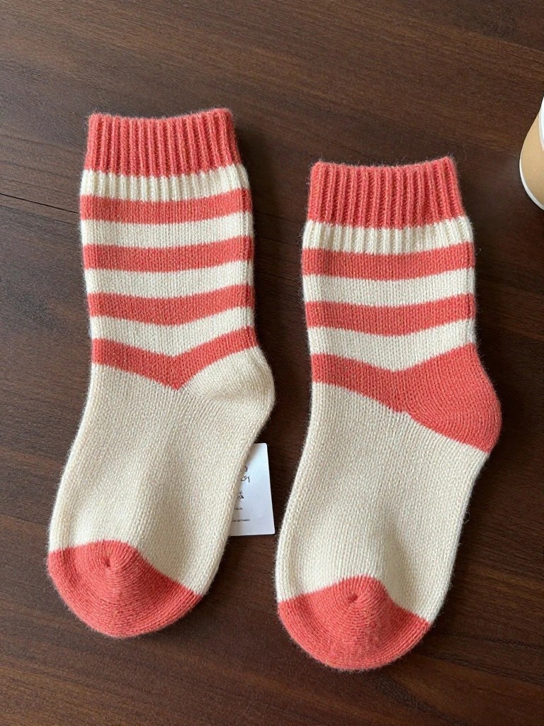 Pair of fuzzy red-and-white chevron-striped knitted ankle socks with ribbed cuffs on a wooden surface.