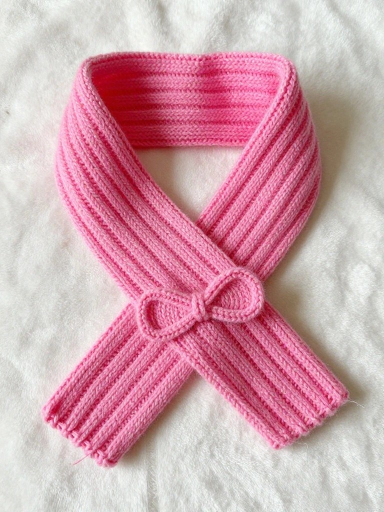 Pink ribbed knitted scarf tied into a bow shape on a white background.