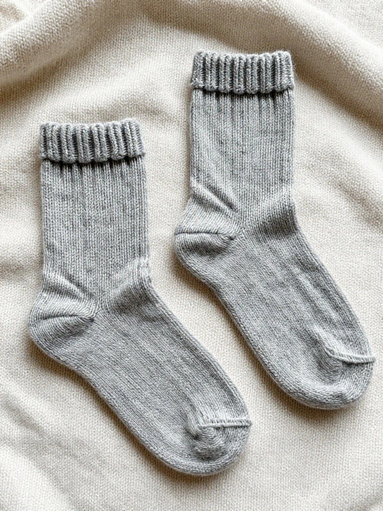 Two light gray ribbed knitted ankle socks laid flat on beige fabric.