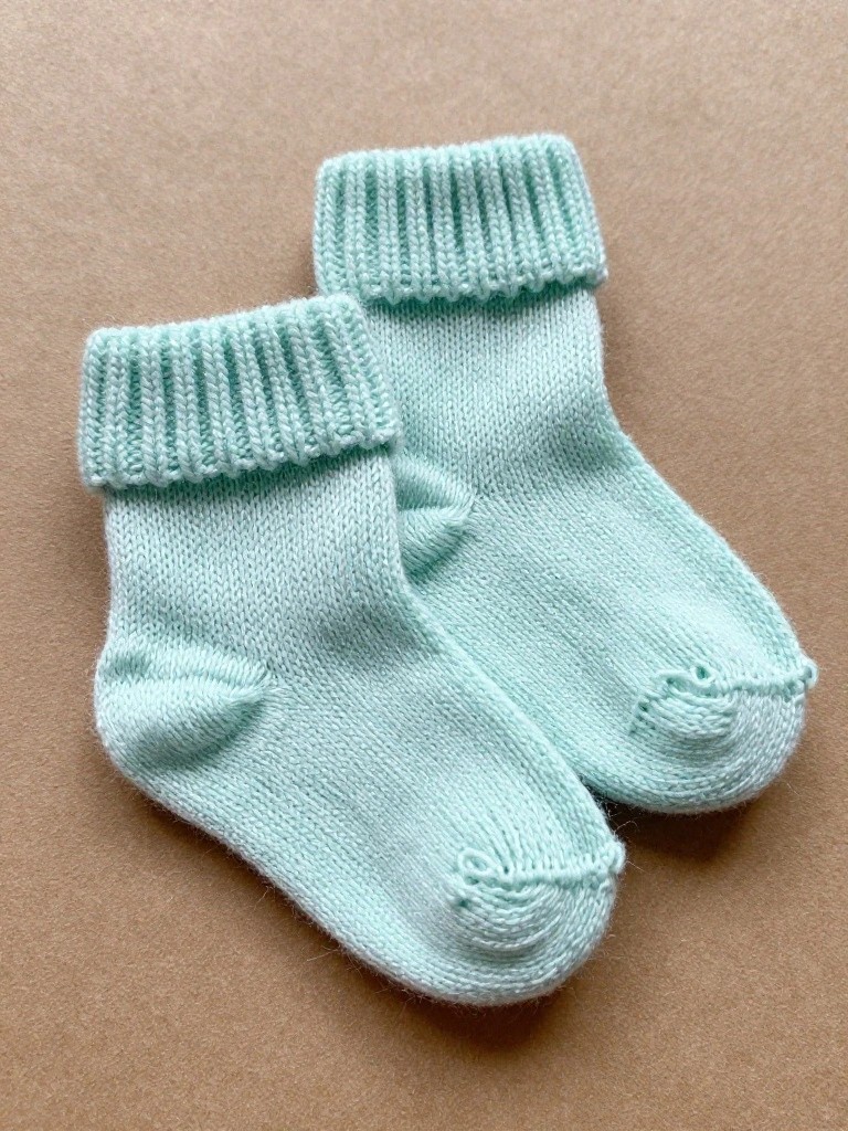 Two light green knitted baby ankle socks with wide ribbed cuffs on beige paper.