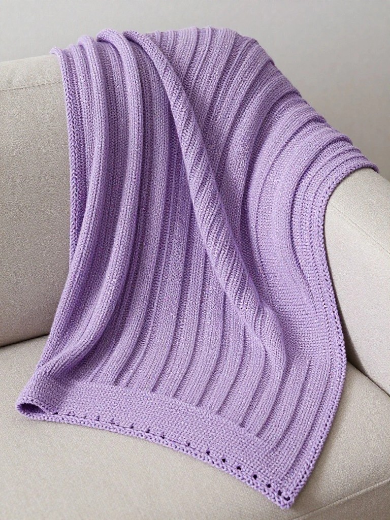 A purple ribbed knitted blanket with vertical ridges and a simple border draped over the arm of a light gray couch.