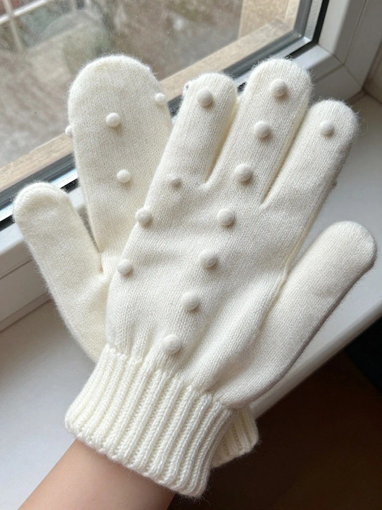 Pair of white fuzzy knitted mittens with rows of small white bobbles on the back of the hands, shown on a windowsill.