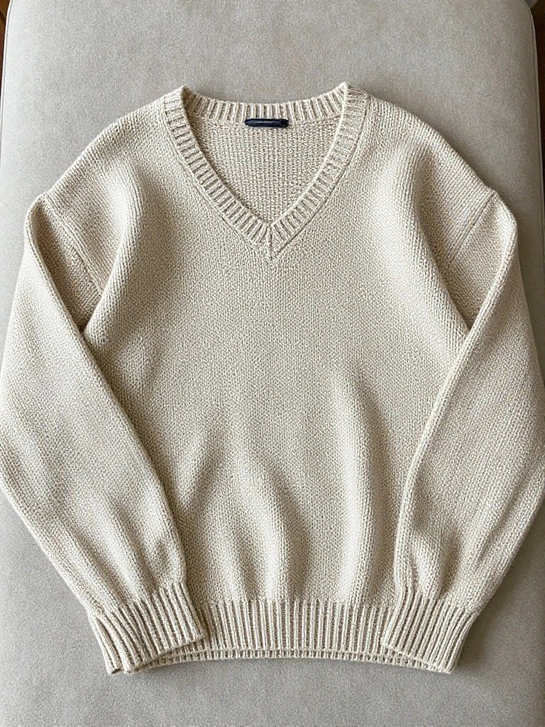 A light beige oversized V-neck knitted sweater laid flat on a beige fabric surface.