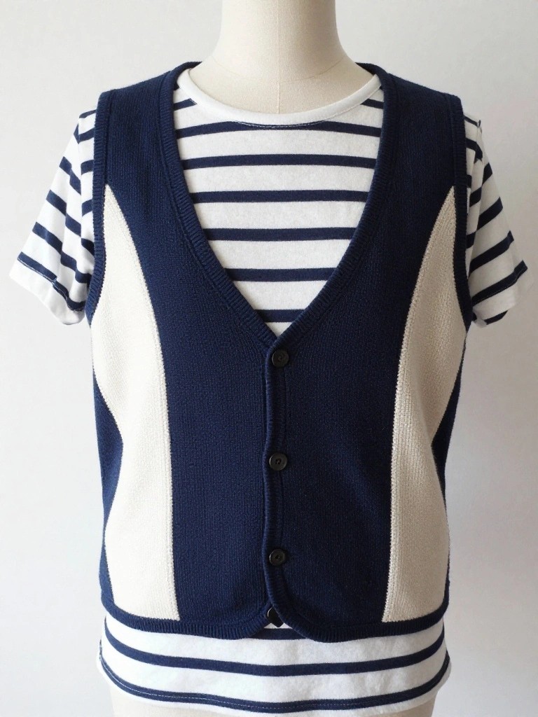 Child-sized navy blue knitted vest with white side panels and button front, layered over a striped shirt on a mannequin.