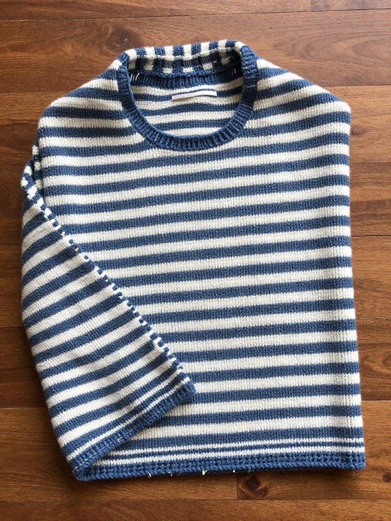 Navy blue and off-white horizontally striped knitted crewneck sweater laid flat on wood with ribbed edges.