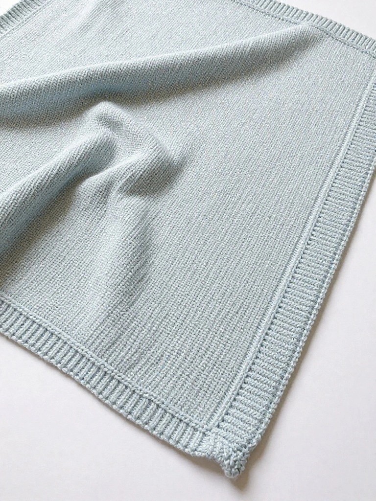 Light blue square knitted blanket with wide ribbed borders on a white surface.