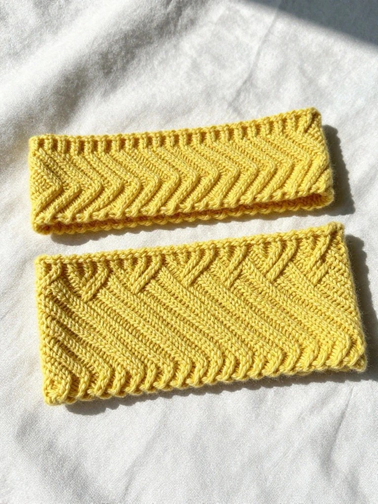 Two yellow knitted headbands, one with horizontal zigzags and one with vertical chevrons, laid flat on white fabric.