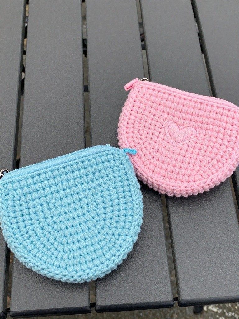 Crocheted pink and blue coin purses with zippers on a bench.