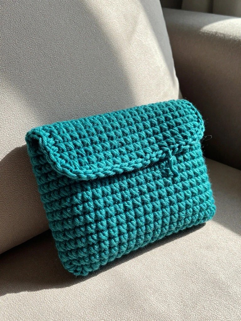 Teal crocheted clutch with flap on light gray upholstery.
