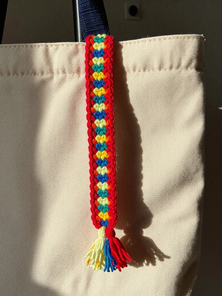 Colorful crocheted bookmark with tassel on beige canvas tote bag.