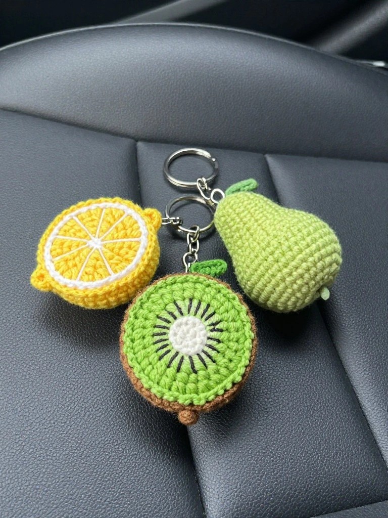 Crocheted lemon, kiwi, and pear keychains on a car seat.