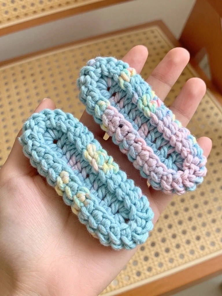 Hand holding two pastel crocheted hair clips with rainbow accents.