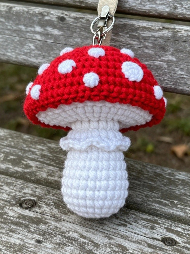 Red-and-white crocheted mushroom keychain hanging from beige strap.