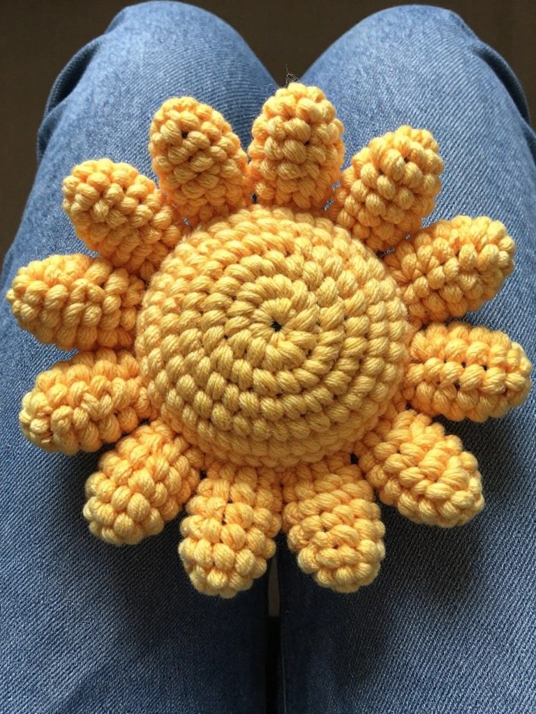 Crocheted yellow sun with spiral center on blue denim jeans.