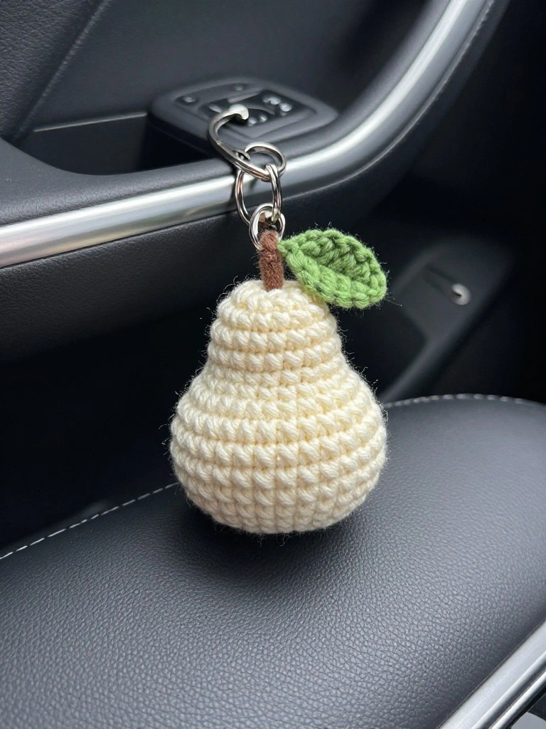 Crocheted cream pear keychain with green leaf on car seat.
