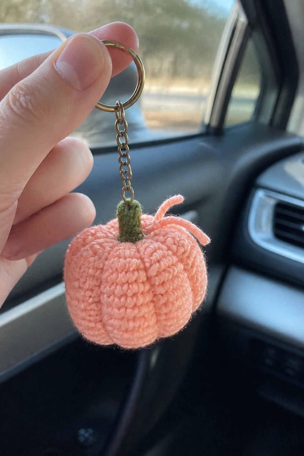 Hand holding pink crocheted pumpkin keychain with green stem in car