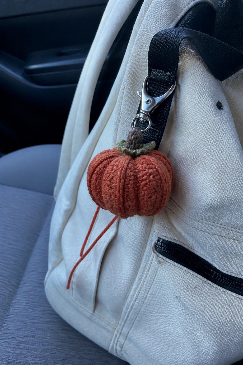 White backpack with orange crocheted pumpkin keychain on black strap in car