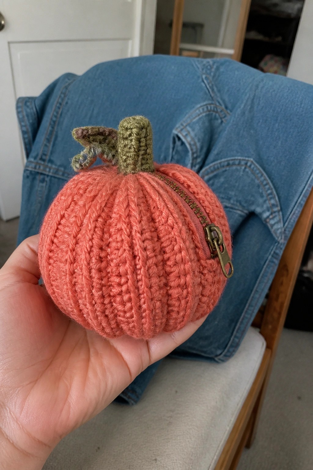 Hand holding crocheted coral pumpkin pouch with green stem and side zipper