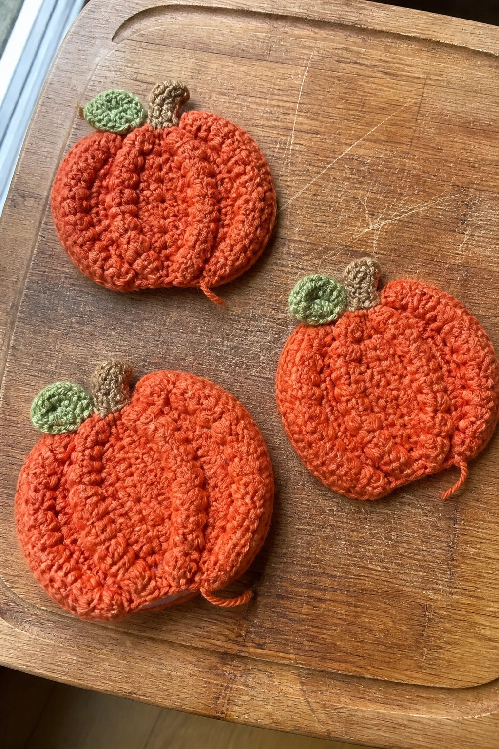 Three orange crocheted pumpkins with green leaves and brown stems on wood