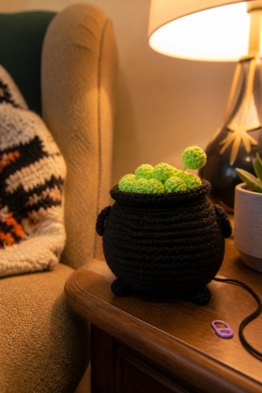Black crocheted cauldron with bright green yarn bubbles on wooden table