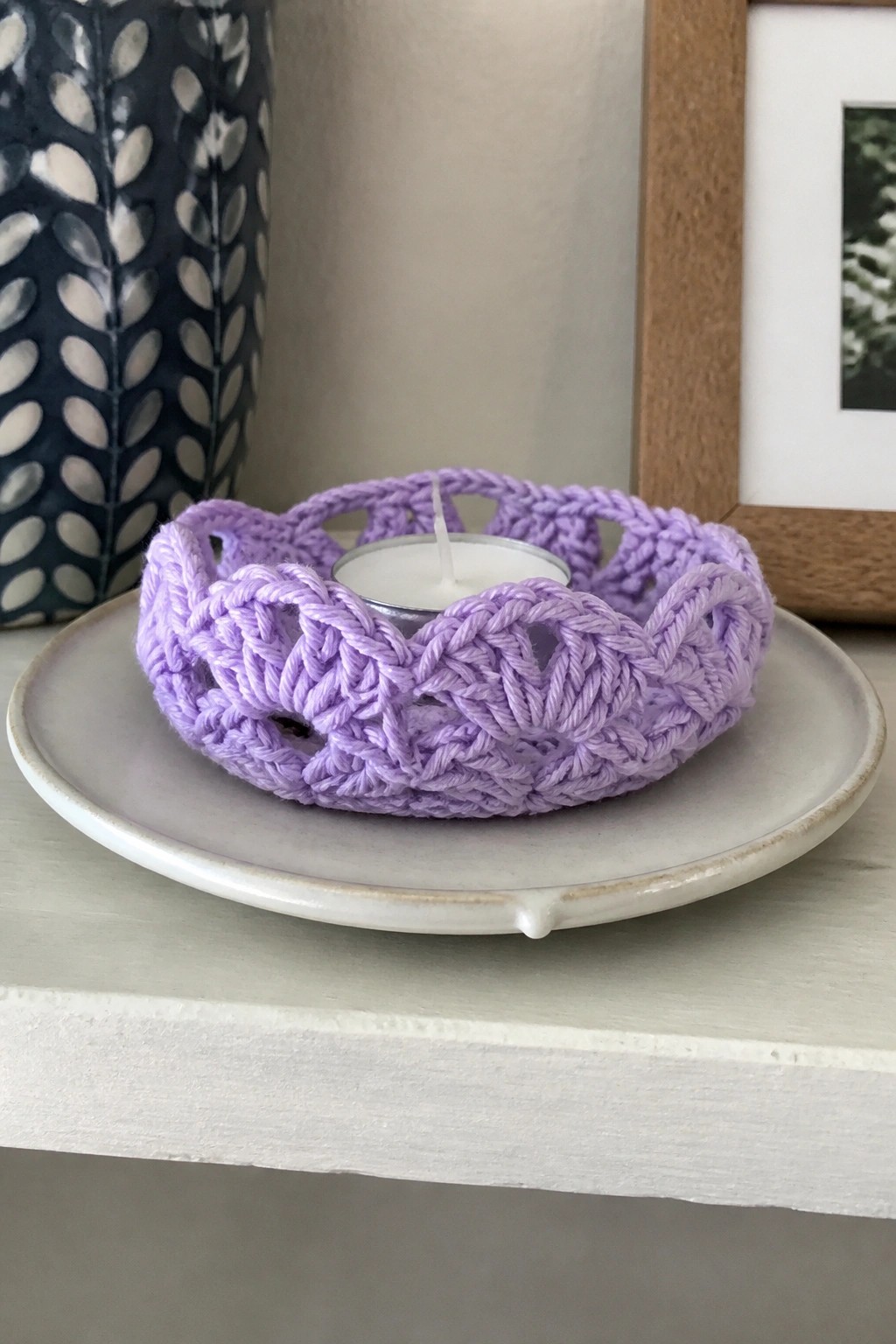 Purple crocheted holder with lit tea light candle on white ceramic plate