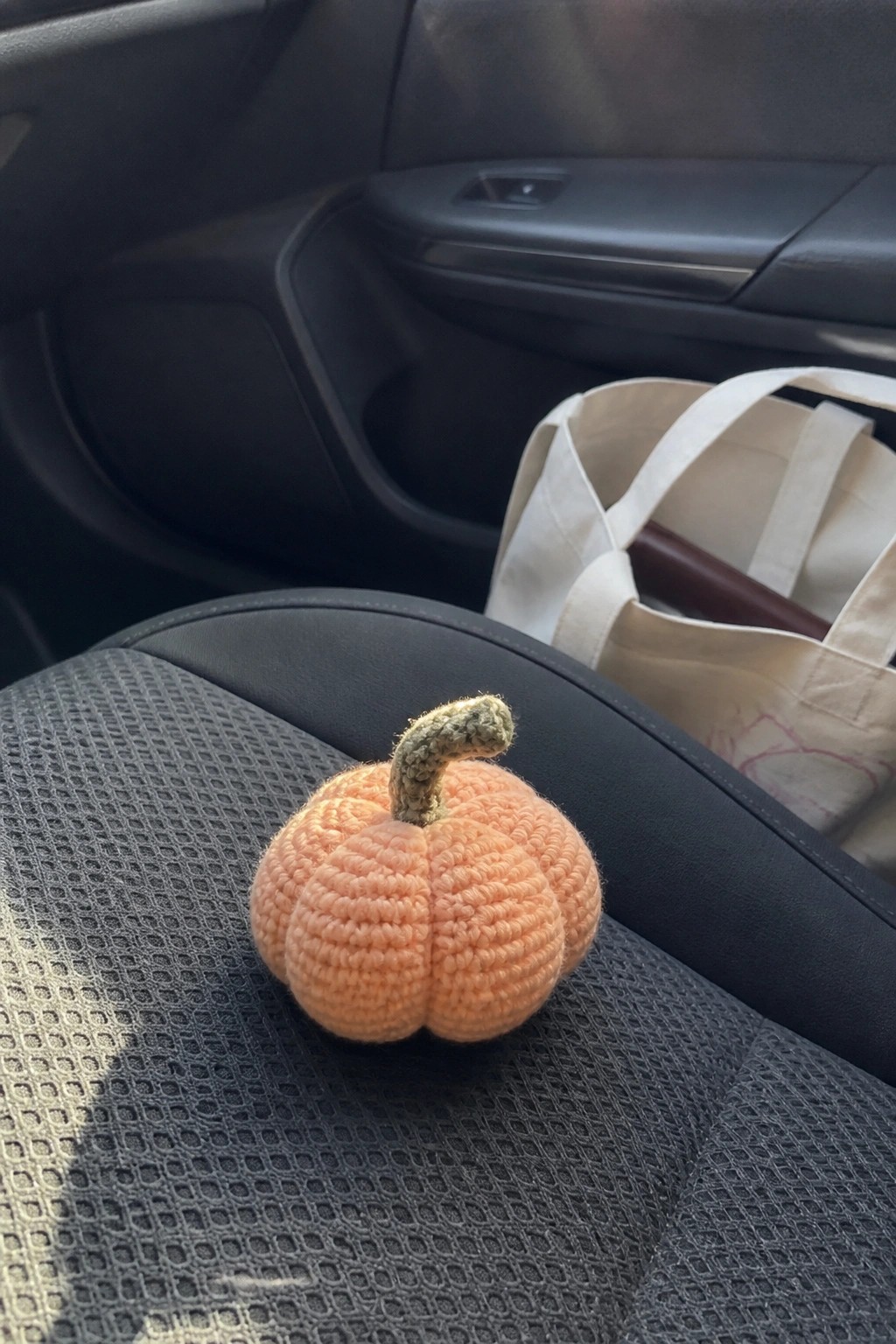 Small orange crocheted pumpkin with green stem on black car seat