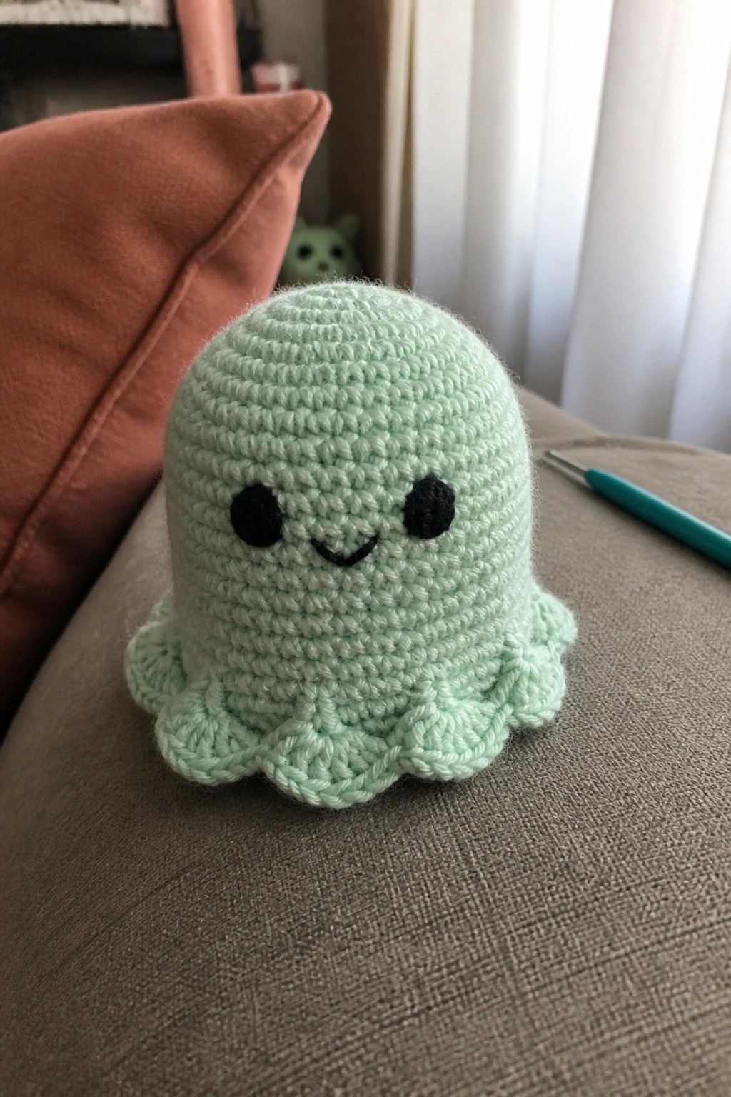 Mint green crocheted octopus plushie with black eyes and smile on gray fabric.
