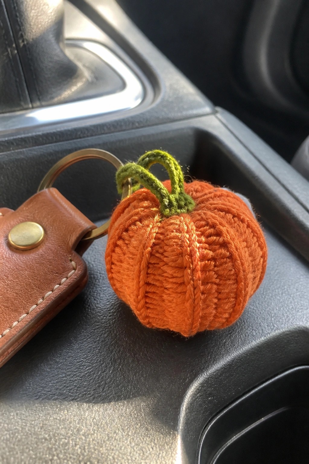 Orange knitted pumpkin keychain with green stem beside brown leather fob in car console