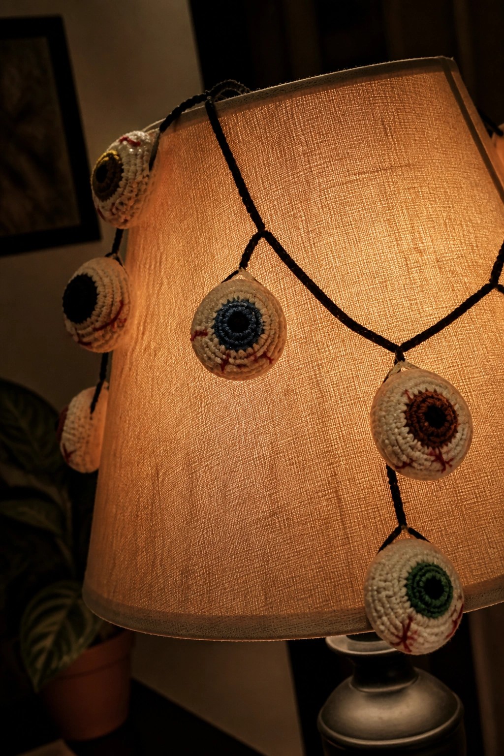 Crocheted eyeballs with colorful irises hanging from a glowing lampshade.