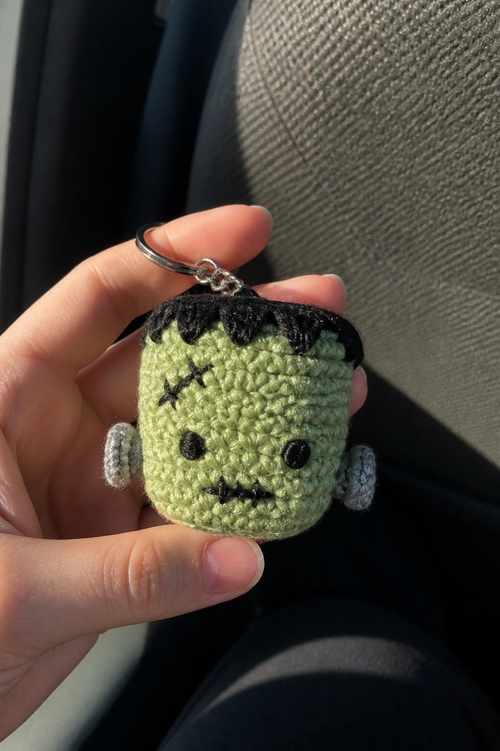 Hand holding crocheted green Frankenstein keychain with black stitches and metal ring.