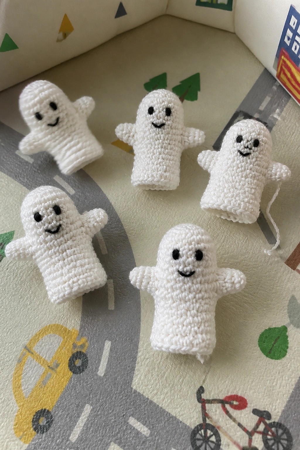 Five white crocheted ghost puppets arranged on a colorful children's play mat