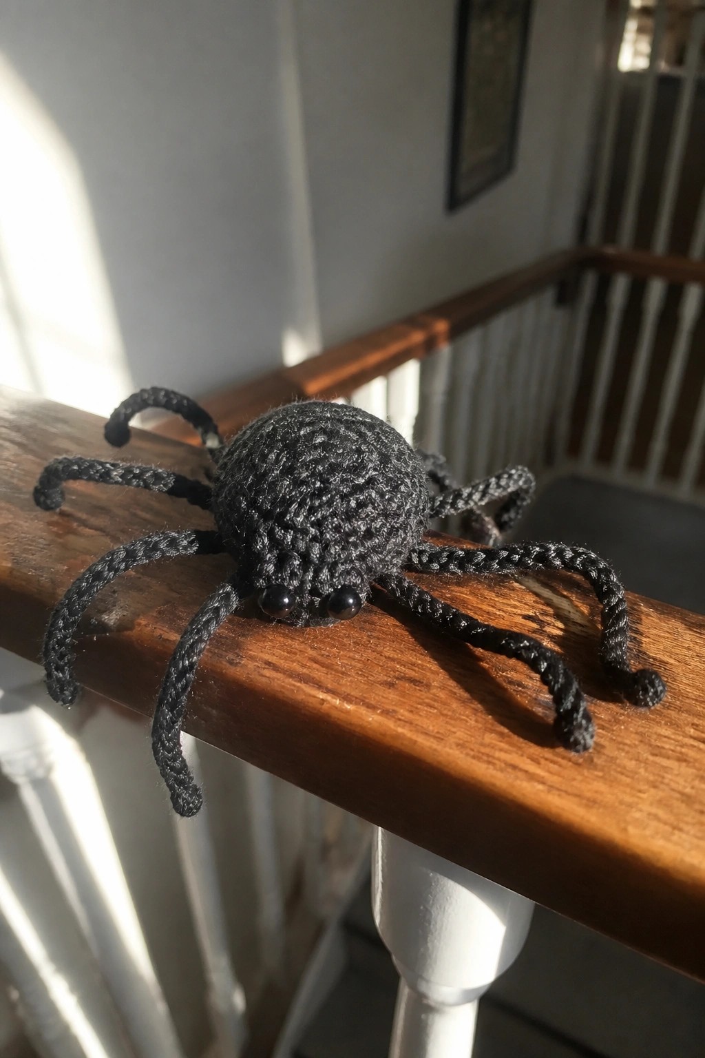 Crocheted black spider with eight legs and shiny eyes on wooden railing