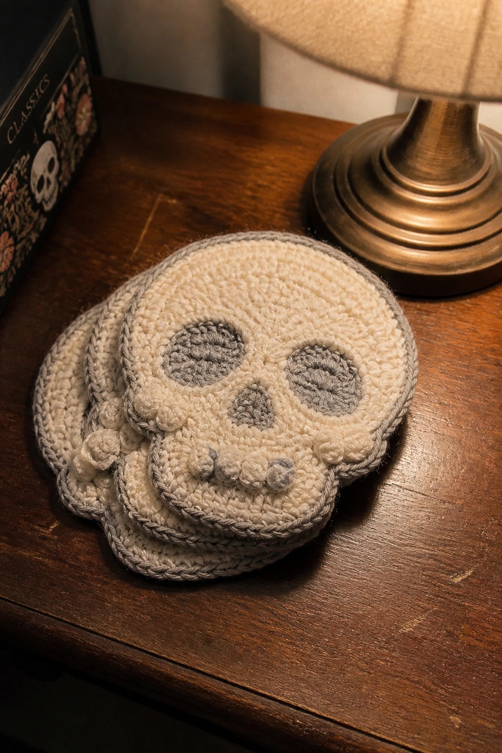 A stack of off-white crocheted coasters with gray skull faces resting on a wooden table.