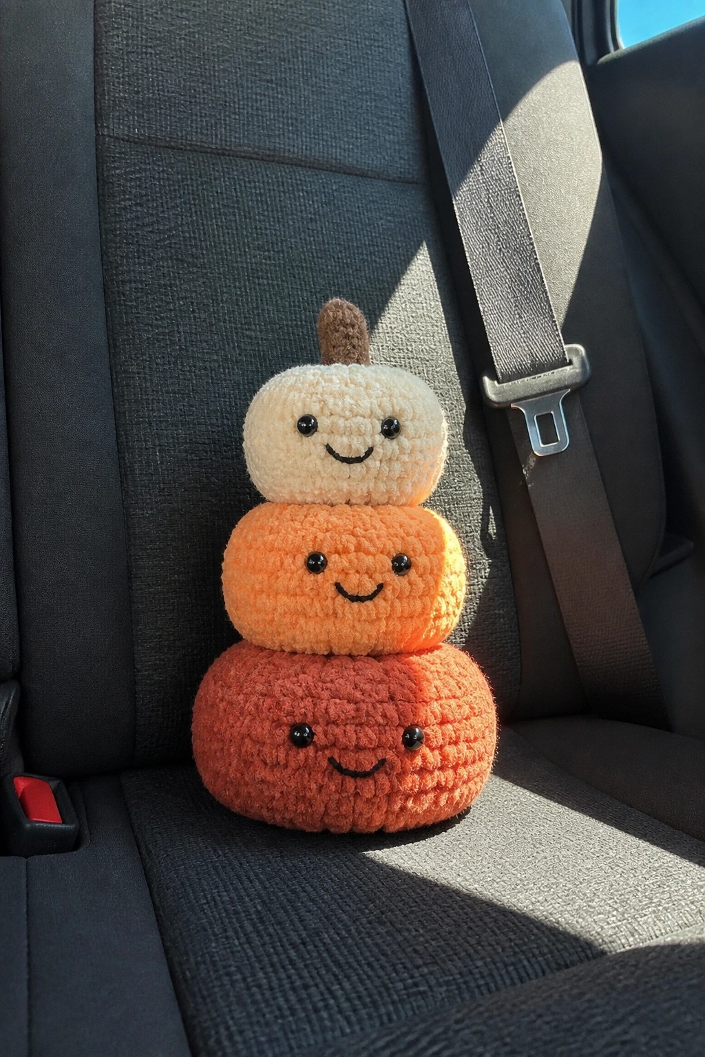 Stacked crocheted pumpkins with faces buckled by seatbelt on car seat