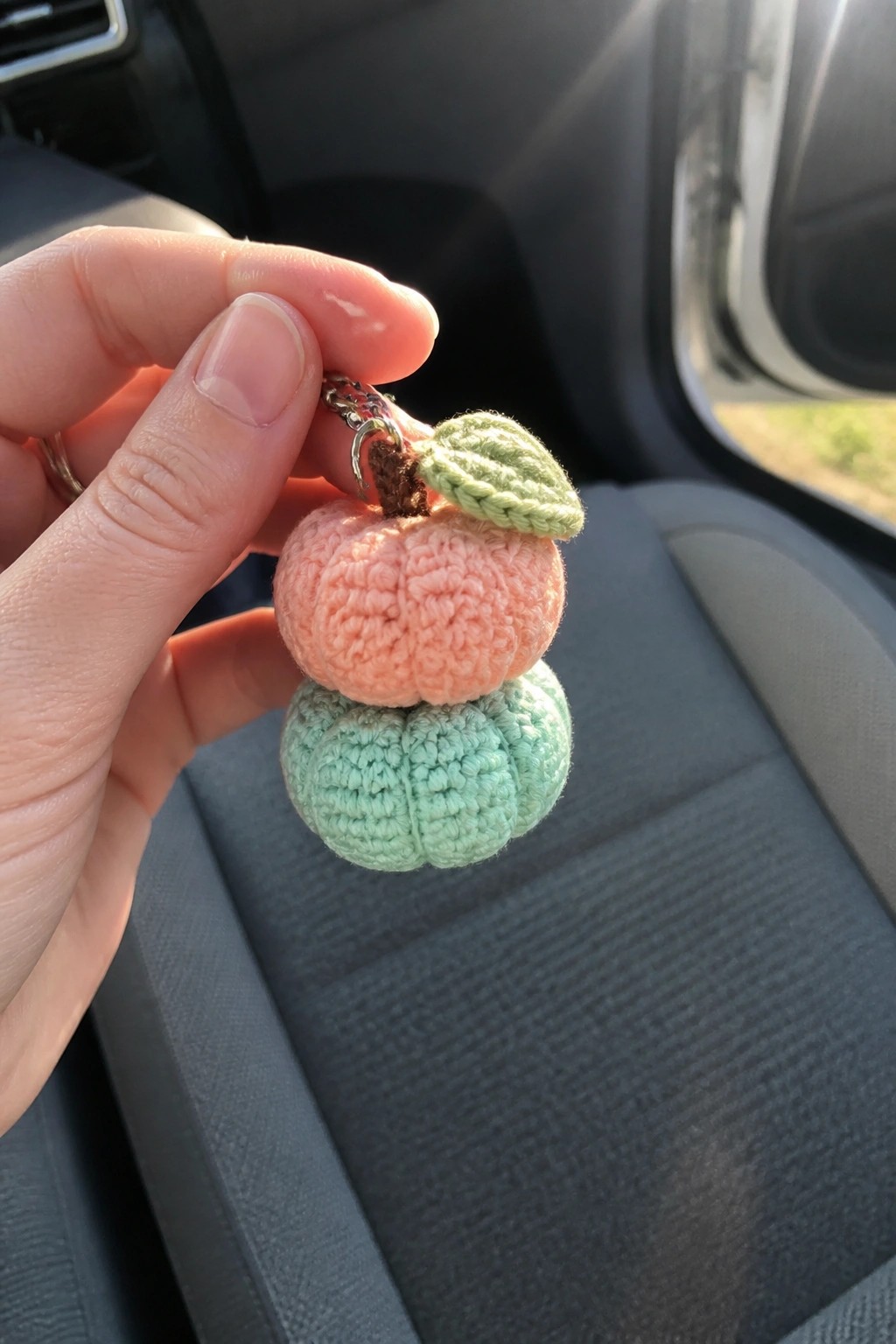 Hand holding crocheted peach and mint green pumpkin keychain with leaf in car