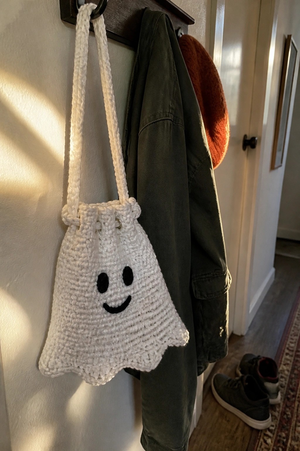White crocheted ghost bag hangs beside green jacket and orange hat on rack