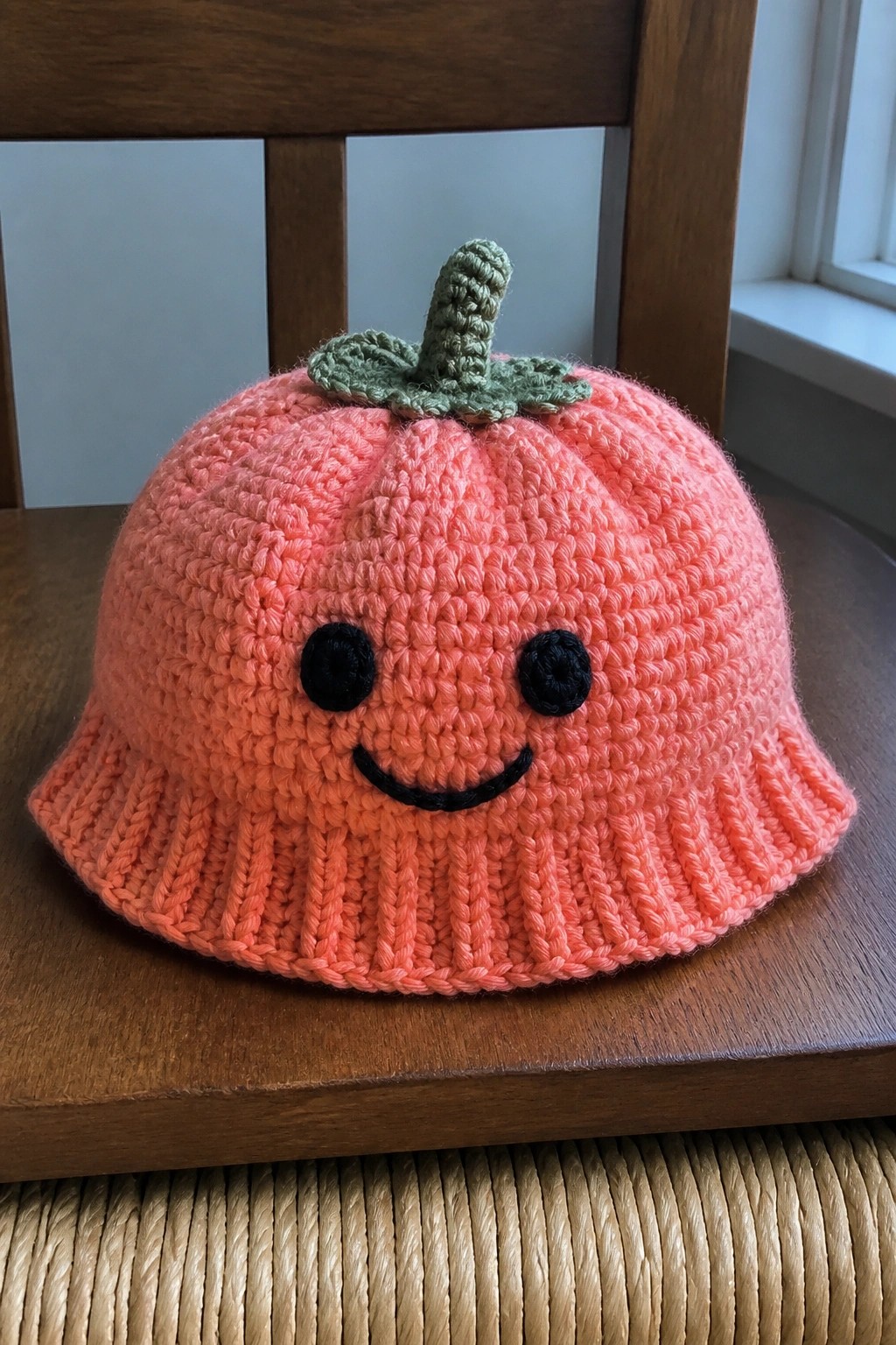 Orange crocheted pumpkin bucket hat with jack-o'-lantern face and green stem on wood