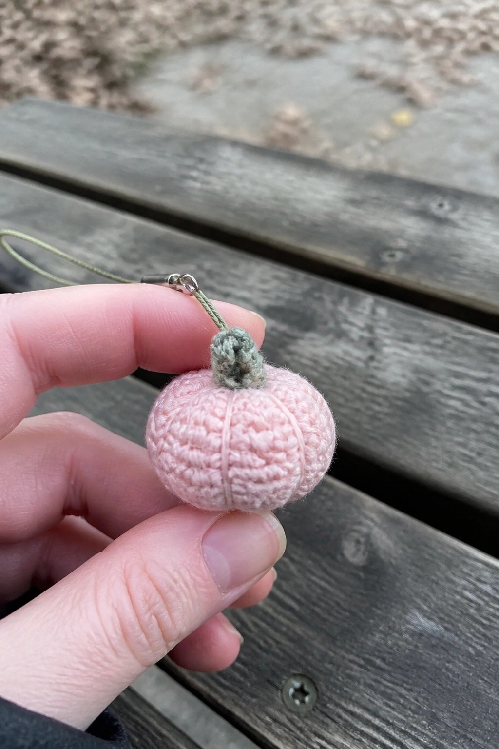 Hand holding pink crocheted pumpkin keychain with green stem on wooden surface