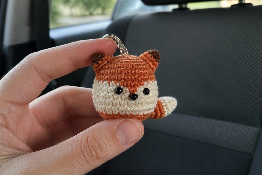 21 Practical Free Fall Crochet Ideas Using Scrap Yarn Hand holding crocheted brown fox keychain with white belly, black eyes, and chain.