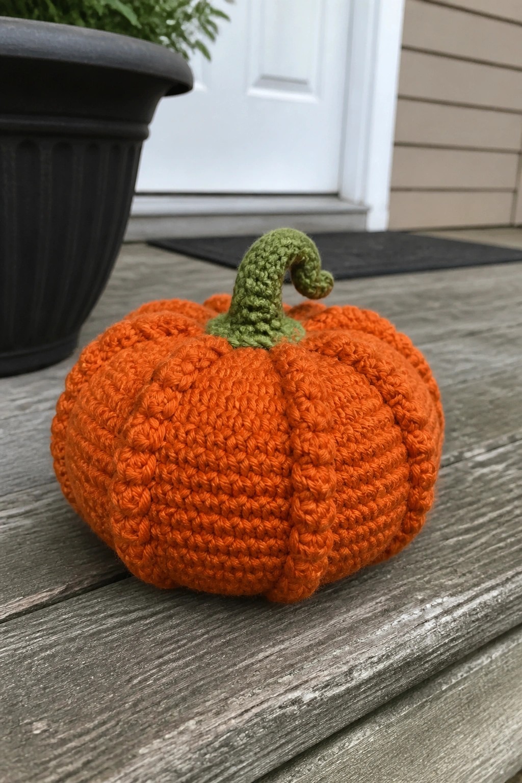 Orange crocheted pumpkin with green stem on weathered wooden porch surface