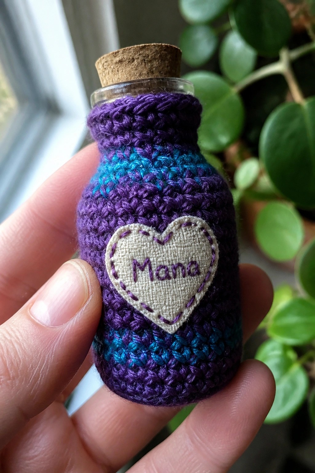 Hand holding a purple-blue crocheted bottle with cork and embroidered 