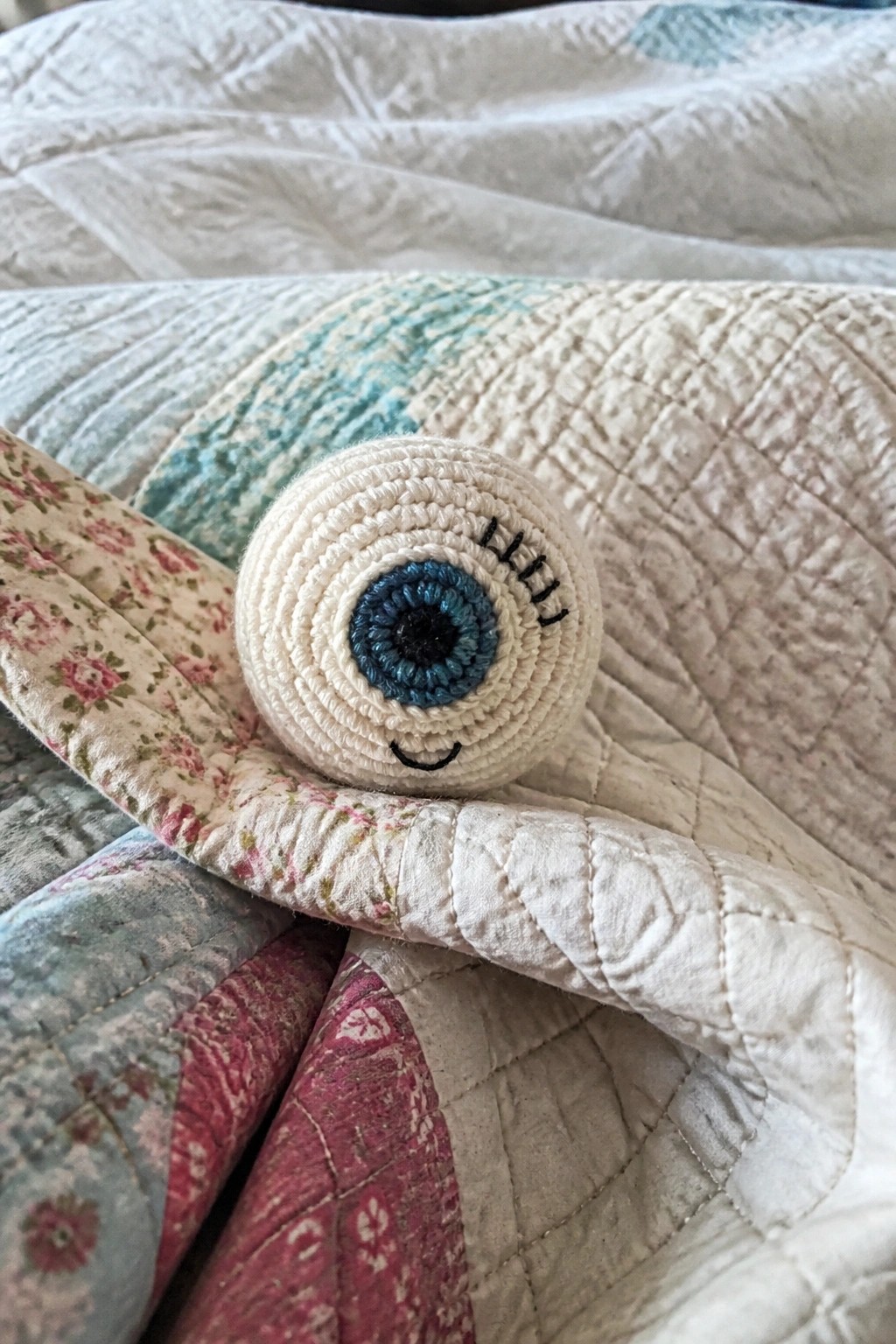 Crocheted white eyeball toy with blue iris on floral quilt.