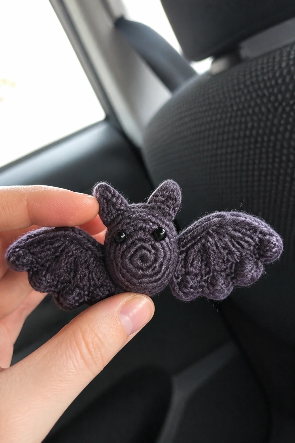 Hand holding purple crocheted bat toy with spread wings inside car.