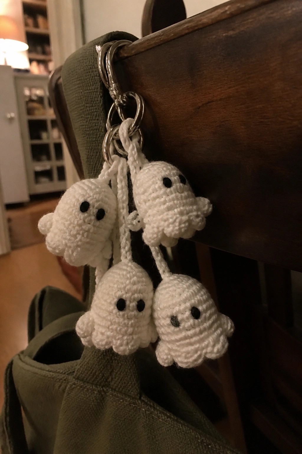 Four white crocheted ghost keychains hanging from rings on a green bag