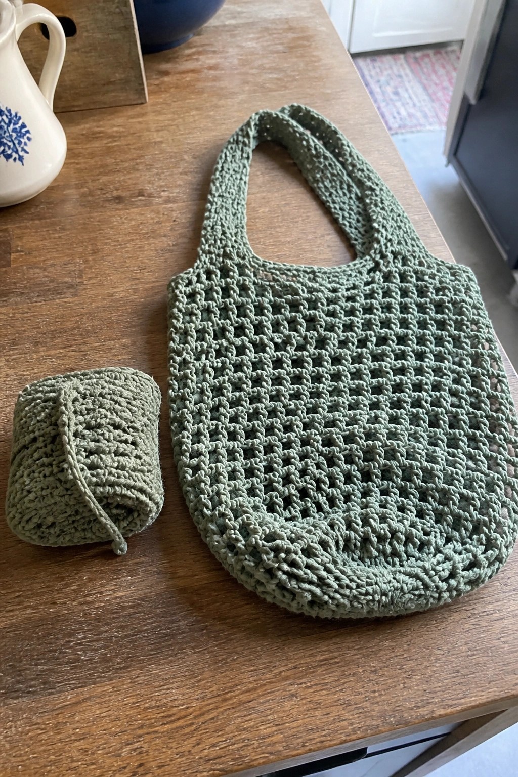 A green crocheted market bag and rolled skein of matching yarn on a wooden table.