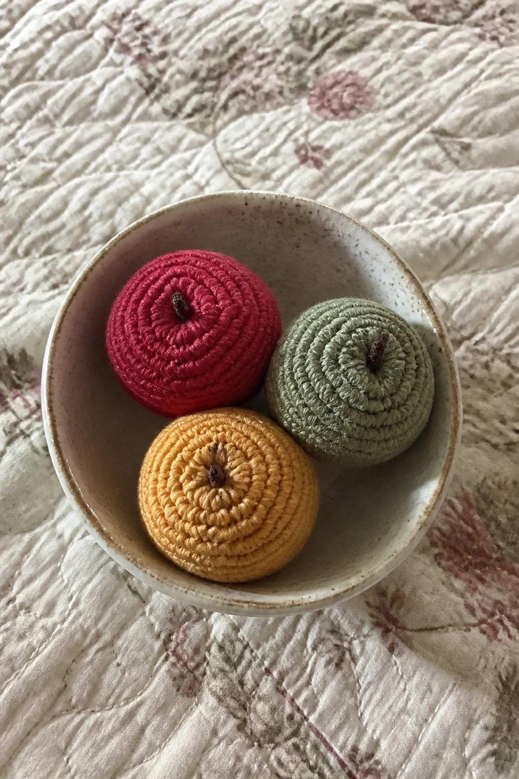 Three crocheted pumpkins in red, yellow, and green inside a ceramic bowl.