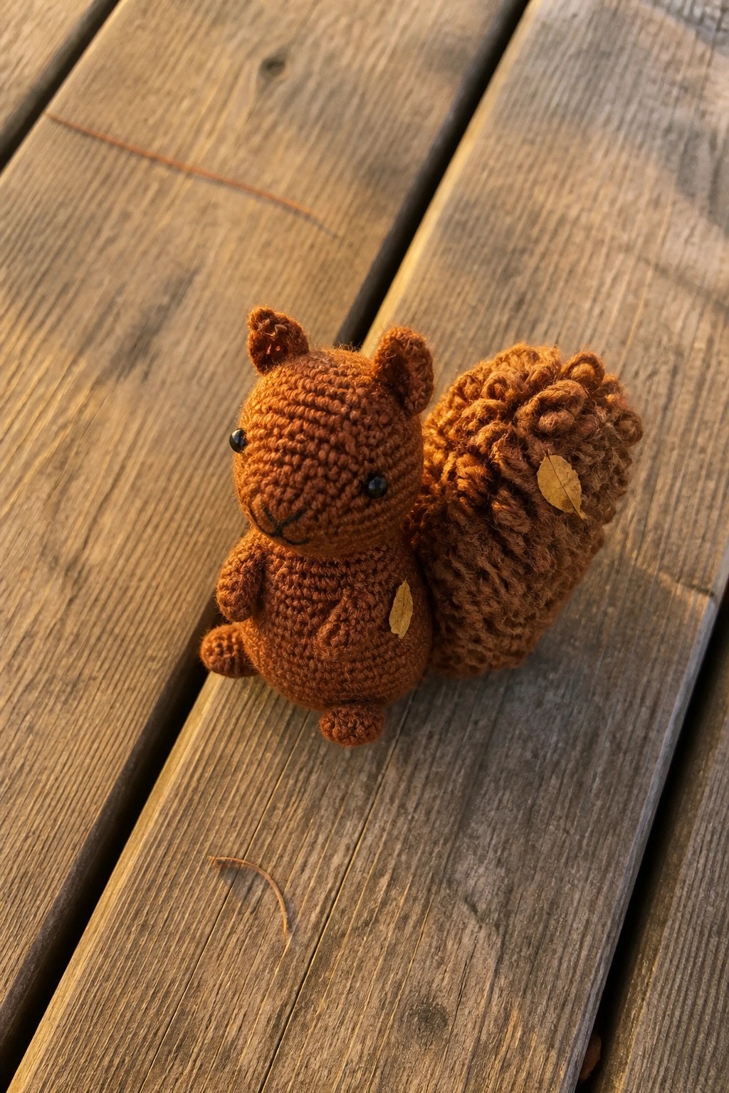 Brown crocheted squirrel with bushy tail and leaves on wooden planks