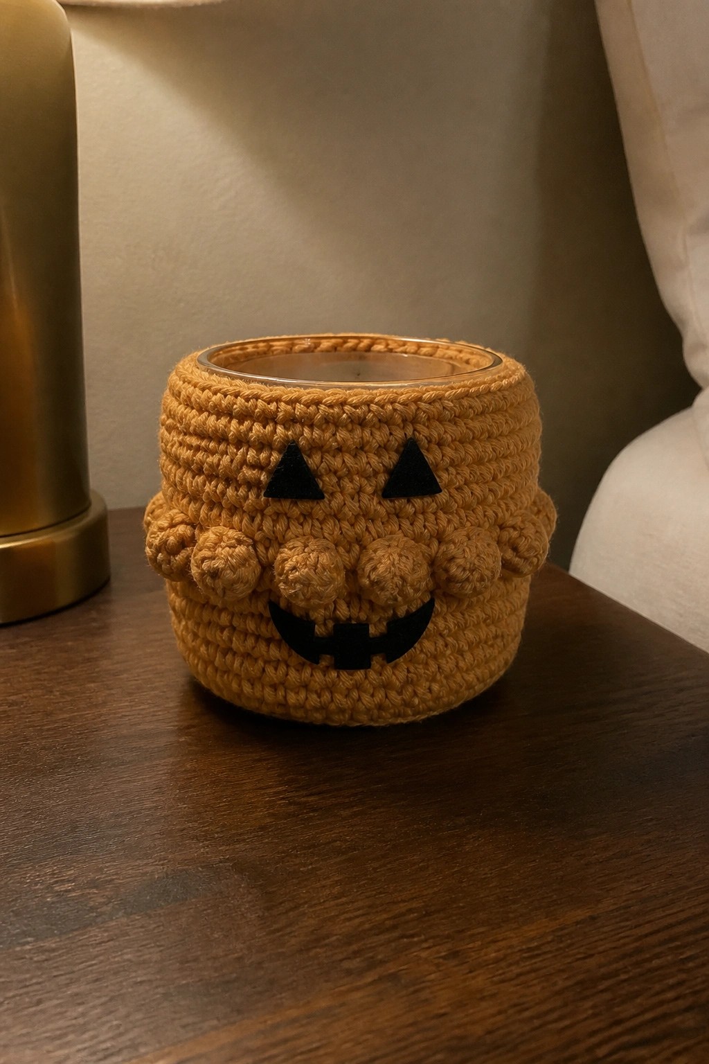 Orange crocheted jack-o'-lantern cozy around glass jar on wooden table
