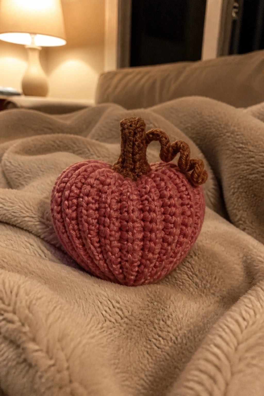 Pink knitted pumpkin with brown stem on soft gray plush blanket