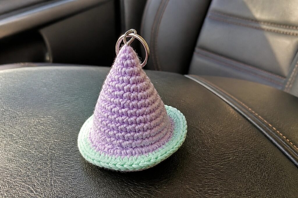 Crocheted purple witch hat keychain with mint brim on gray car seat